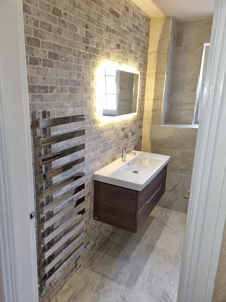 Stone-effect tiled en-suite with backlit mirror, chrome ladder rad and walnut wall-hung vanity