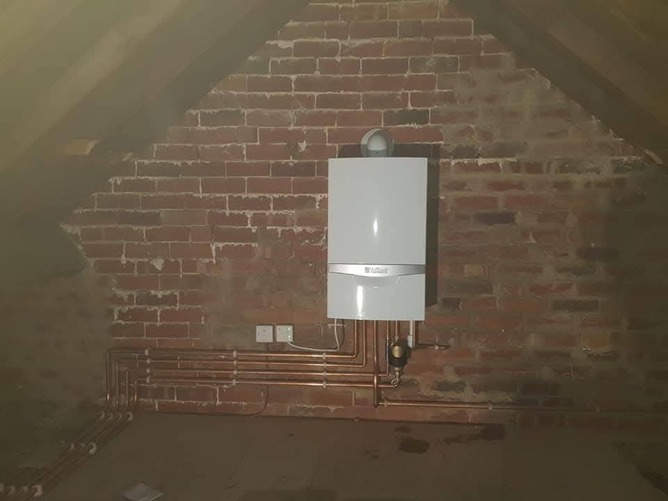Vaillant combi boiler installed against an exposed brick wall with copper gas and flow-return pipework, replacing a solid-fuel system