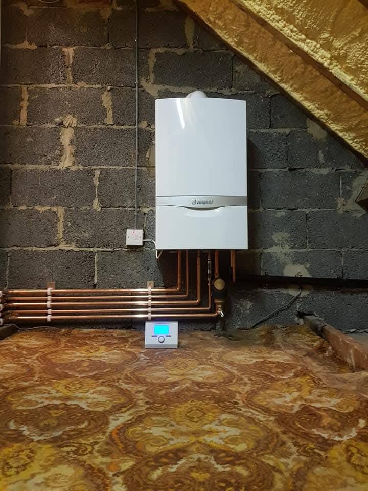 Vaillant boiler installed on a concrete block gable wall with a 5-port copper manifold below and Honeywell smart stat